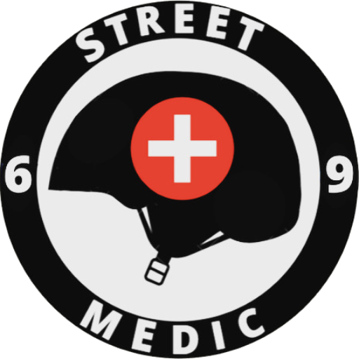 Logo Street Medic 69 : Un casque noir avec un croix blanche sur fond rouge. Le tout entouré d'un cercle noir avec Street Medic 69 inscrit dessus.